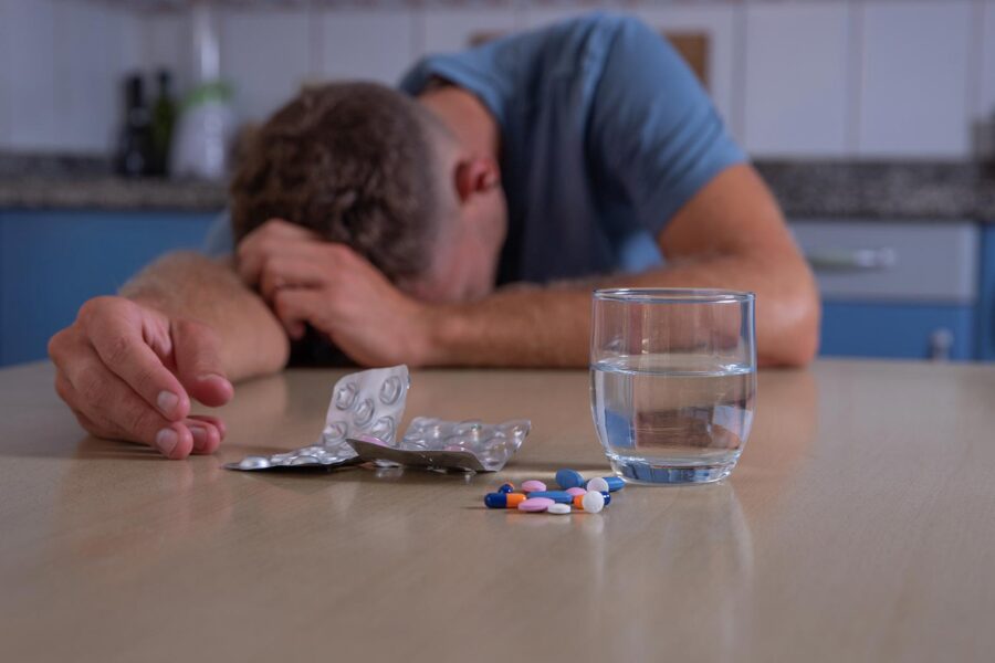Adderall Withdrawal: A man with his head down on a table with several pills and a glass of water in front of him.