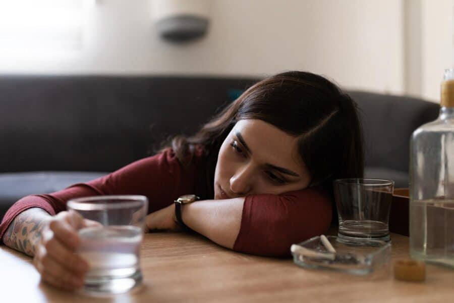 Gabapentin Withdrawal: A woman leaning with her head down on a table reaching for a glass of water
