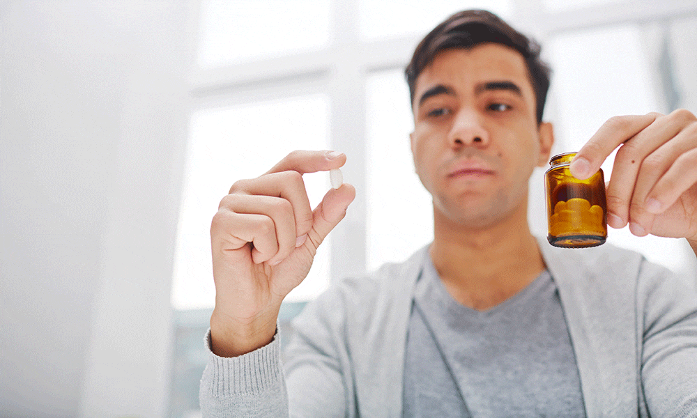 A man examining a pill he holds between two fingers
