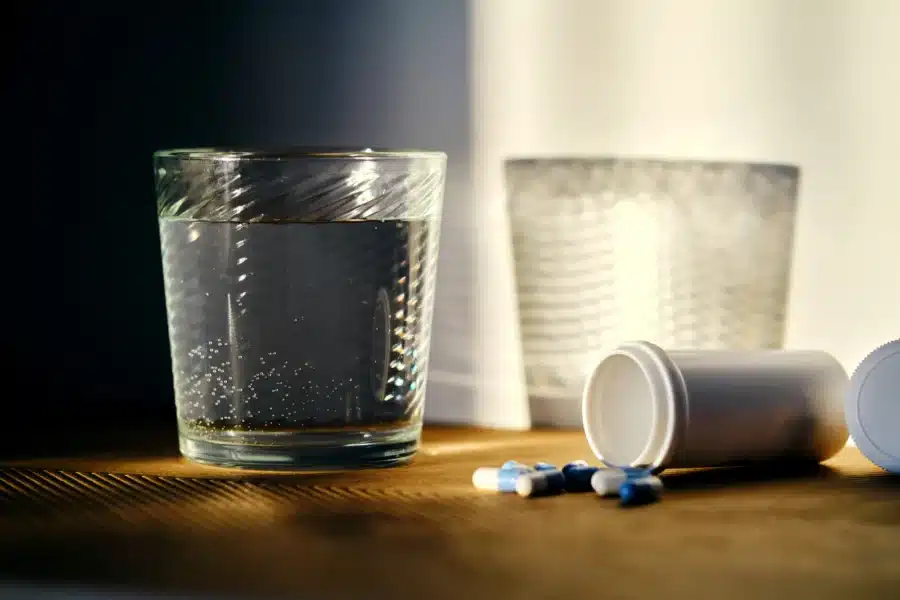 Codeine Allergy Symptoms: Two glasses of water sitting on a table with a pill bottle that has fallen over will pills spilling out.