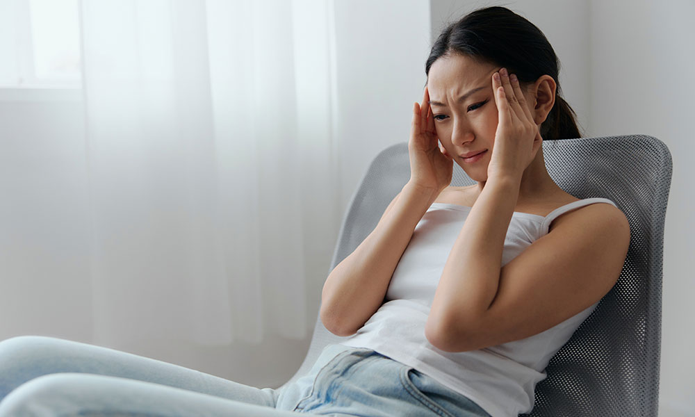 Woman sitting in a chair, holding her temples, appearing to have a headache