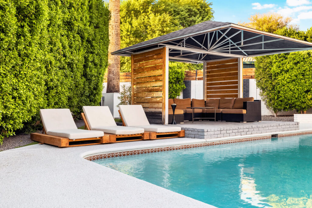 11-622-W-Palmaire-Ave-071-1 Poolside scene with three lounge chairs and a wooden gazebo featuring a brown couch set.